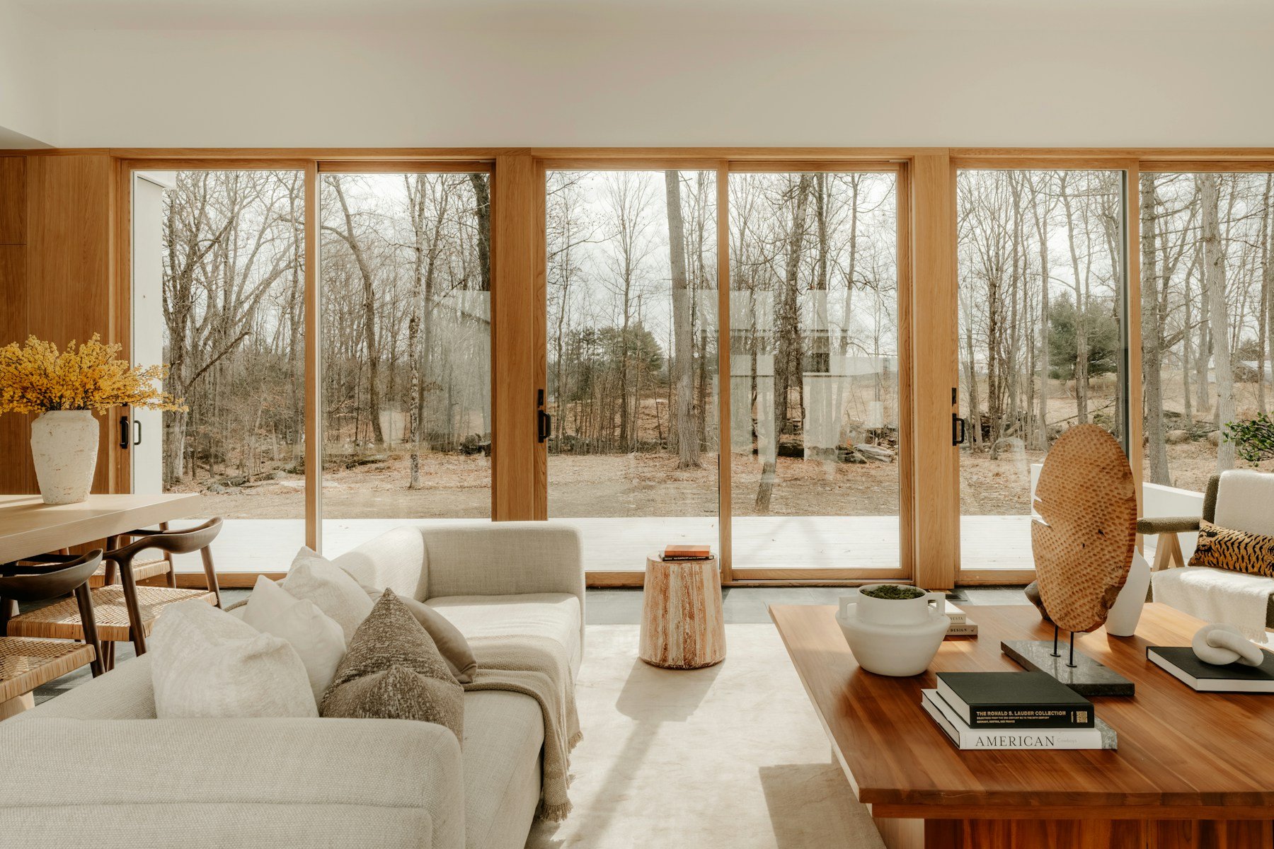 Warm contemporary living room with ivory sofas, timber-framed windows and a woodland view.